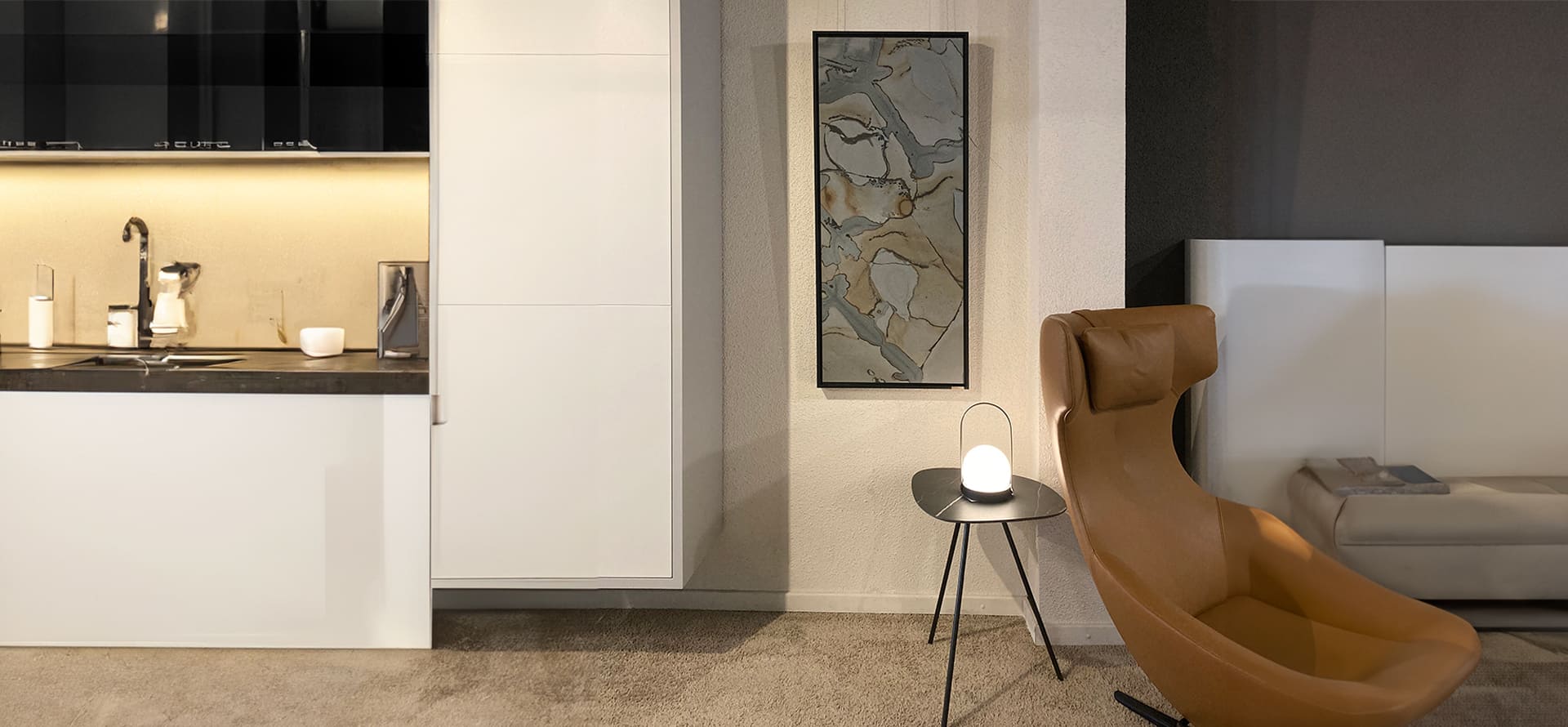 Eine moderne Wohnausstellung mit einer Küchenzeile und einem innovativen Sessel hinter dem ein Natursteinkunstwerk von STEINBILD hängt